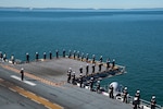 Sailors and Marines in uniform stand at the ship’s perimeter.