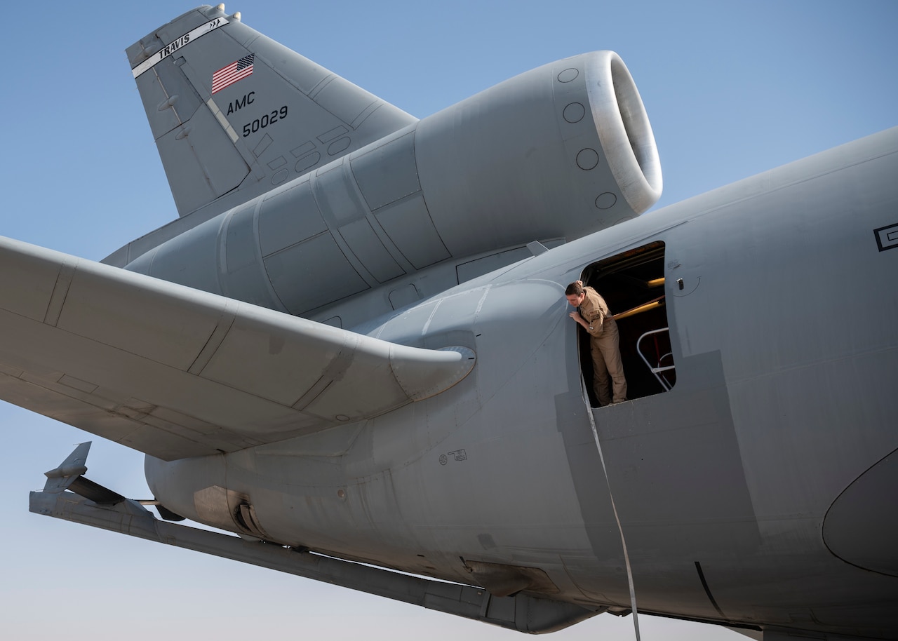 An airman looks out a door toward the rear of an aircraft.