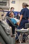 two dental workers talk with a patient sitting in a reclining dental chair.