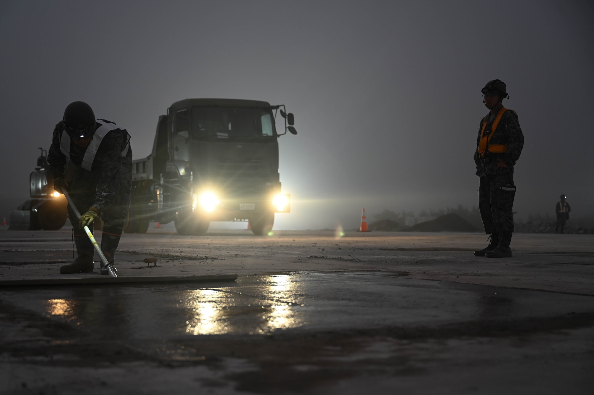 A Japan Air Self-Defense Force Airman smooths out wet concrete at night.