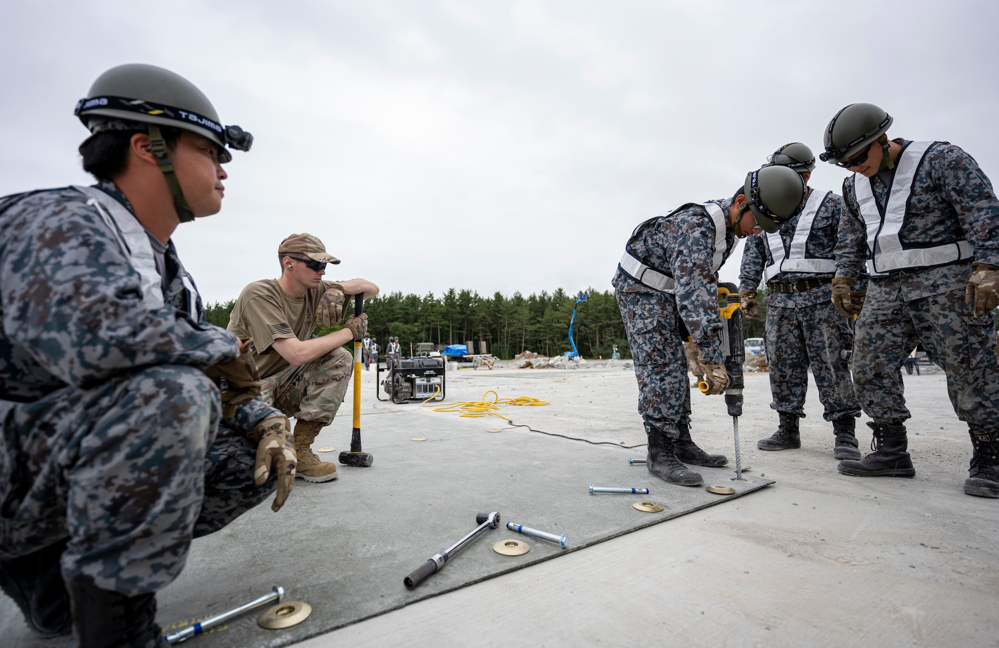 Japan Air Self-Defense Force Airmen assigned to the Western Air Civil Engineering Group anchor a fiber-reinforced polymer mat during a bilateral live fire exercise.