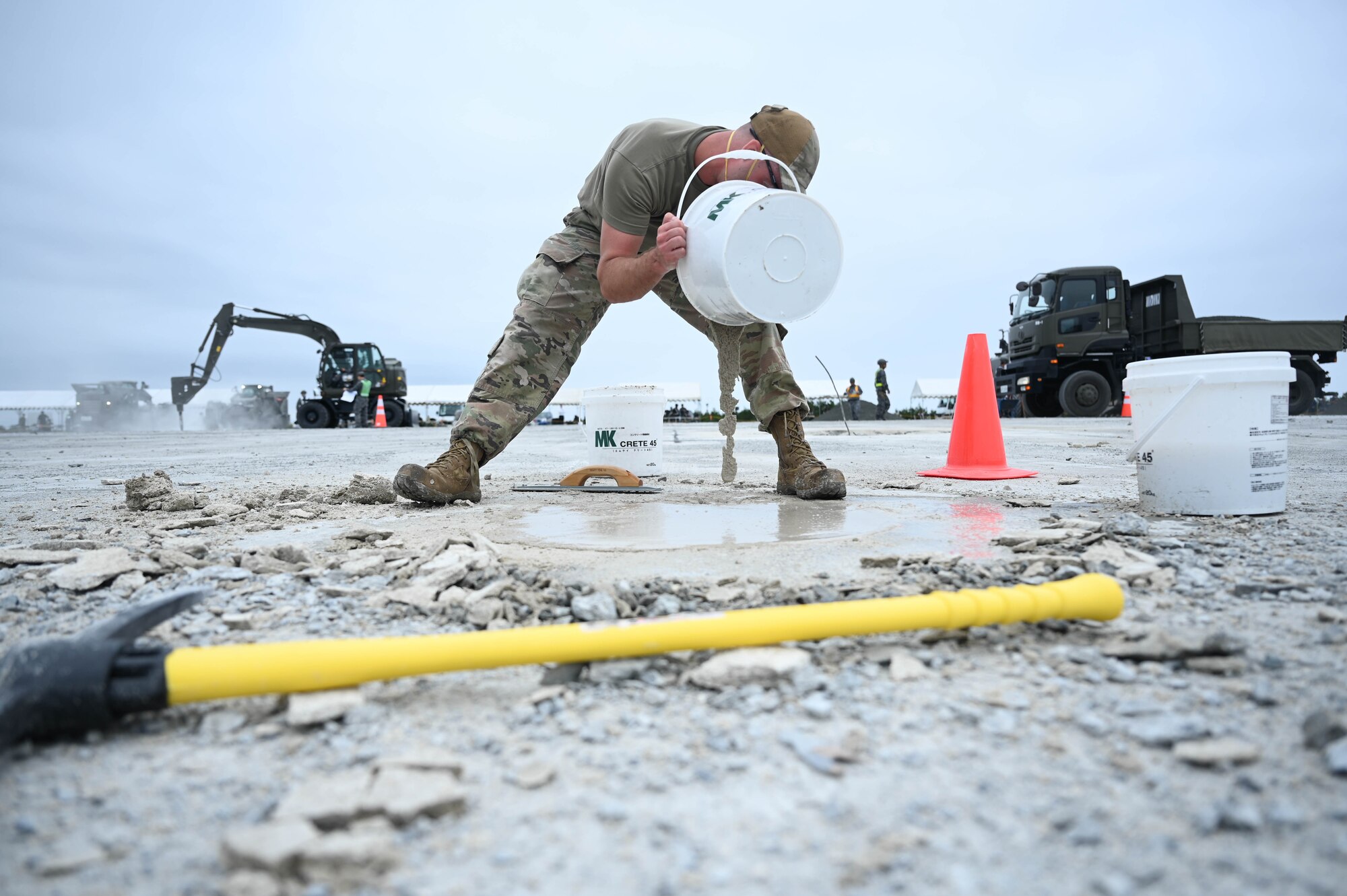 A U.S. Air Force Airman assigned to the 18th Civil Engineer Group pours quickset concrete into a spall during a bilateral live fire exercise.