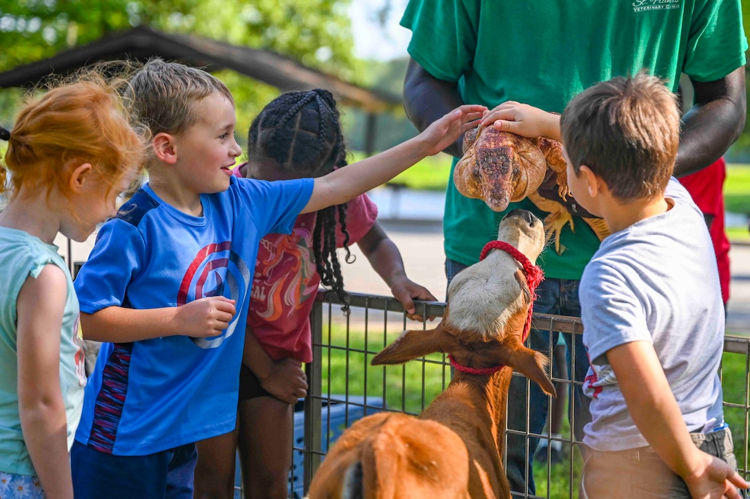 Children pet a lizard as another animal sniffs the lizard from below.