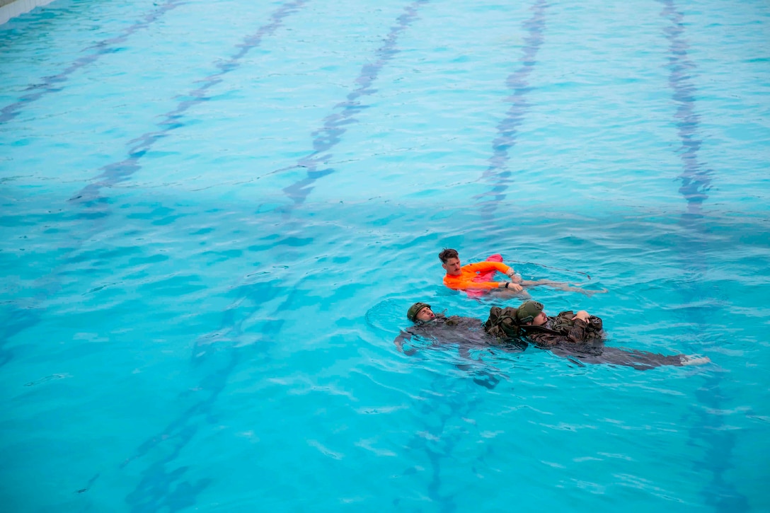 A Marine uses a flotation device while floating on his back in a pool next to two others.