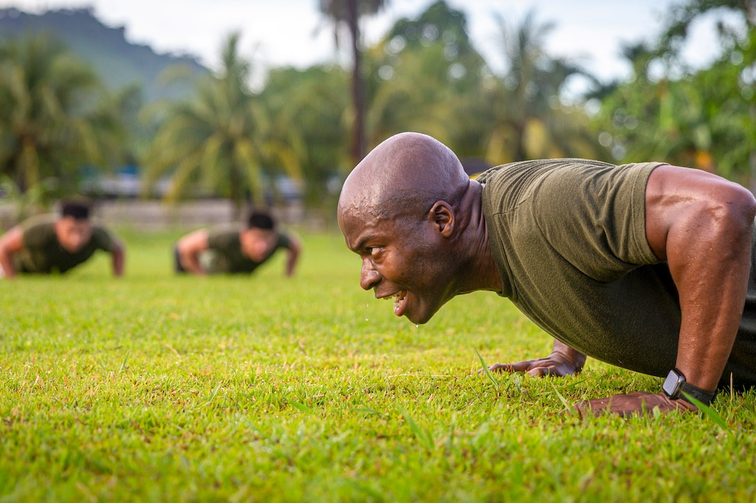 A Marine performs pushups in front of two blurred Marines also performing pushups in the background.