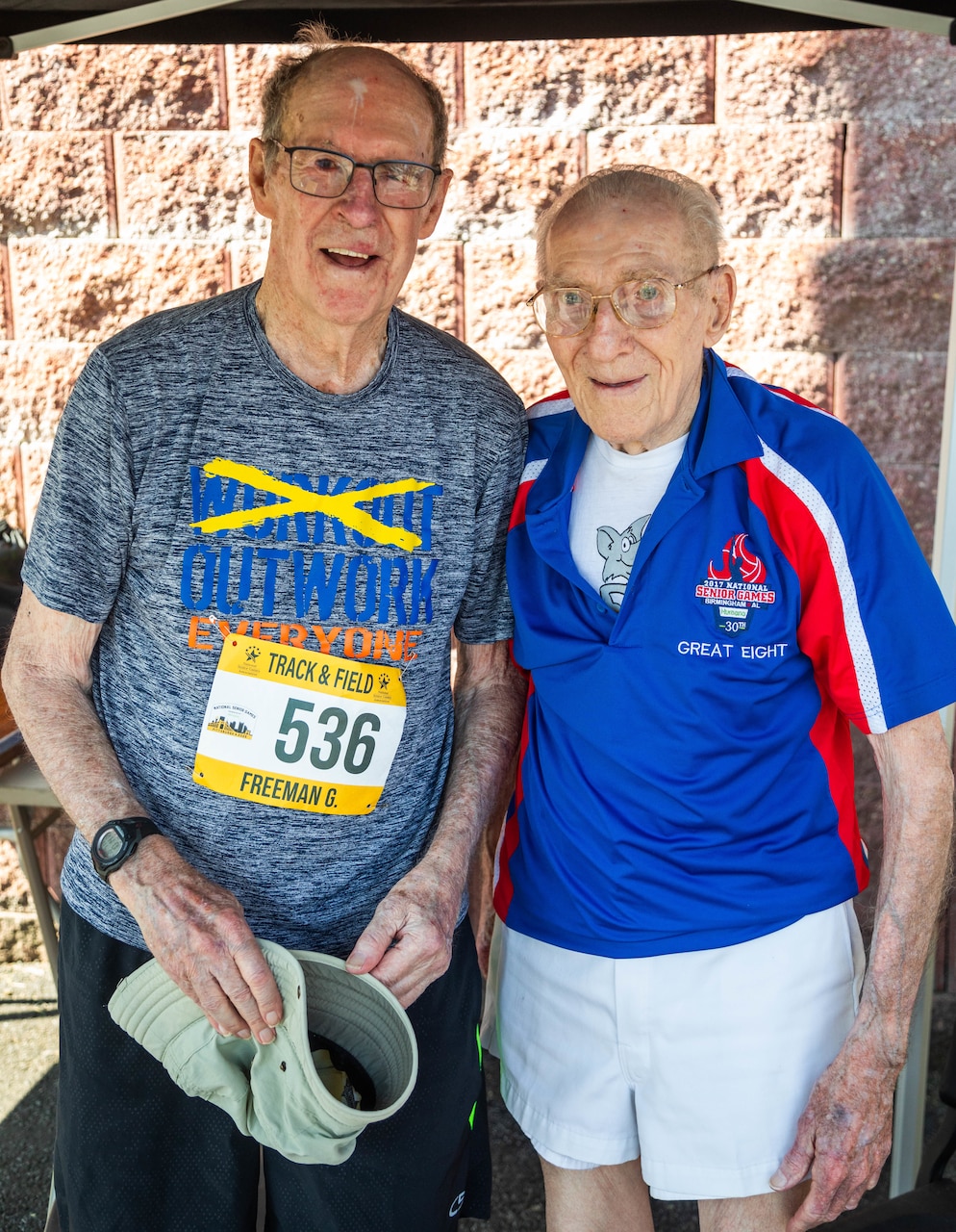 Two men in track and field gear pose for a photo.