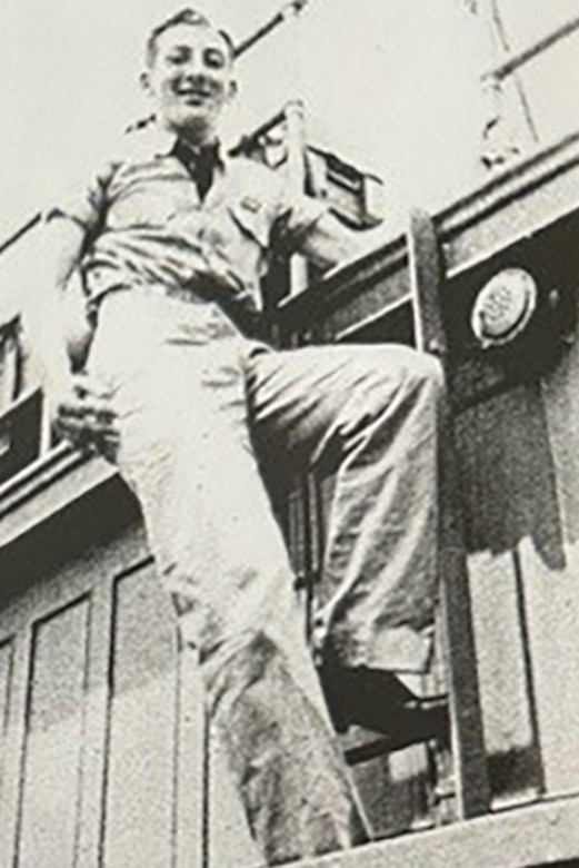 A smiling man stands on a ship’s ladder.