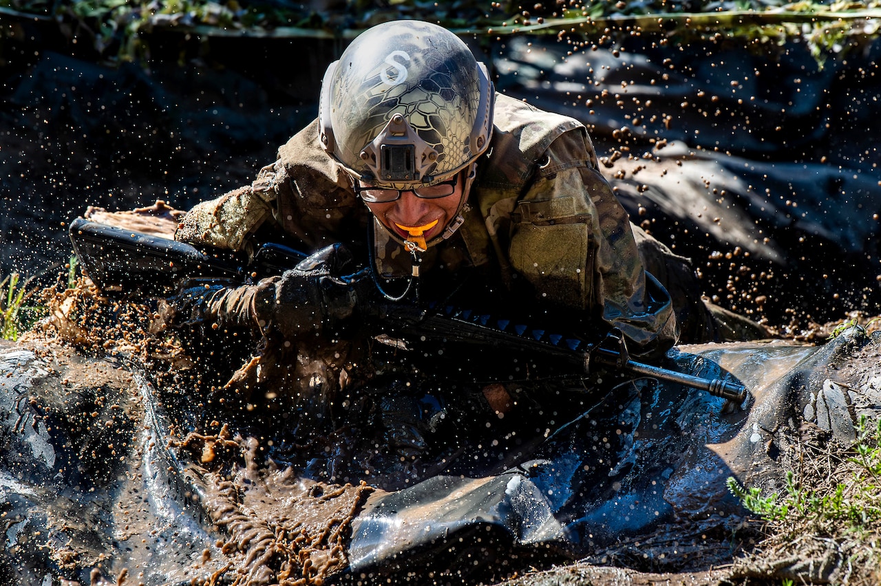A cadet crawls through water while holding a weapon.