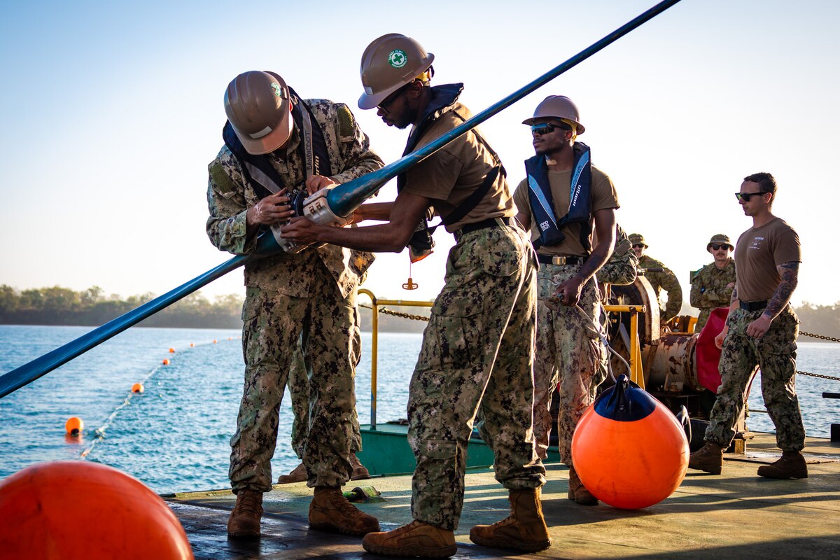 Sailors handle a collapsible pipeline aboard a vessel.