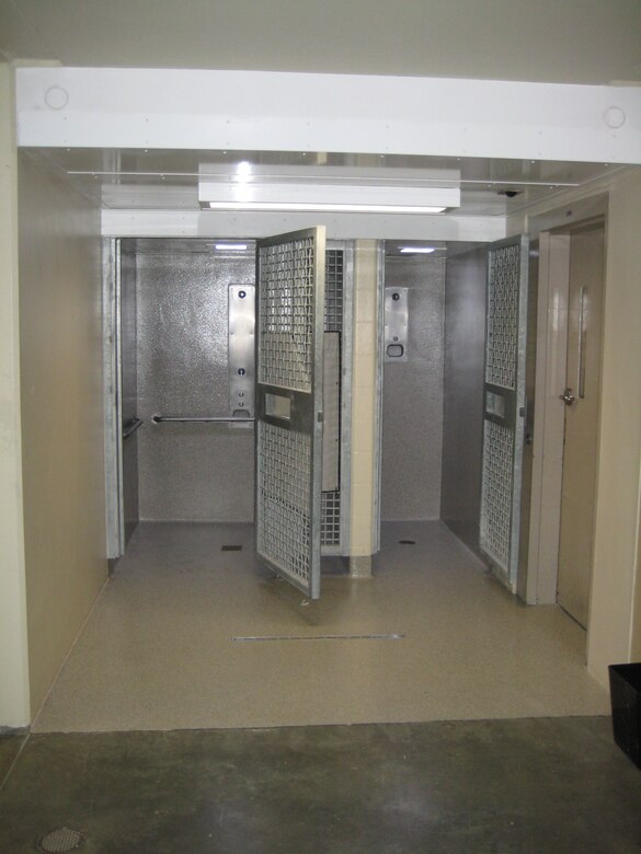 Two shower stalls are open with steel wire doors and concrete floors.