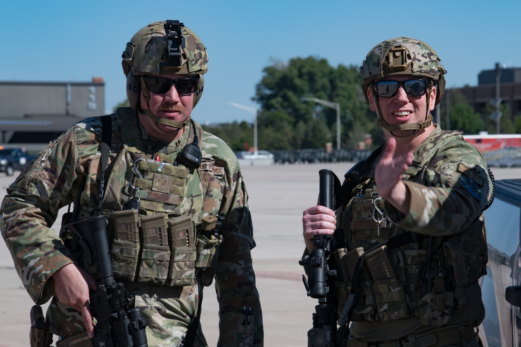 Two Airmen holding rifles, one of them gesturing with his hand, both of them wearing helmets.