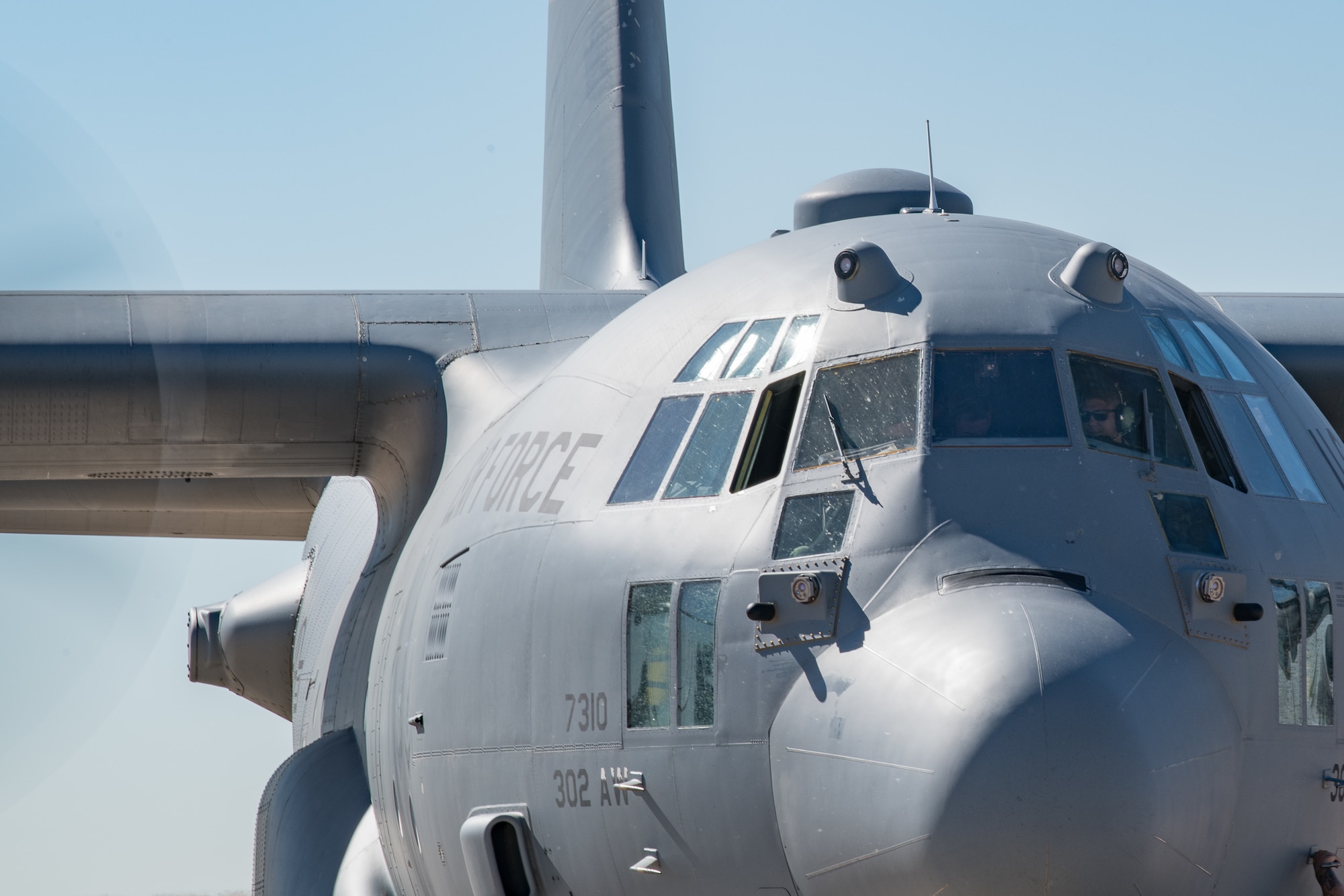 A C-130 aircraft with someone inside of the crew compartment and half of a propeller spinning.