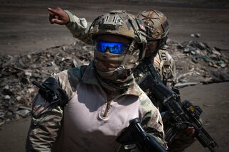 Airmen in tactical gear, cropped above waste in photo are in a barren landscape.