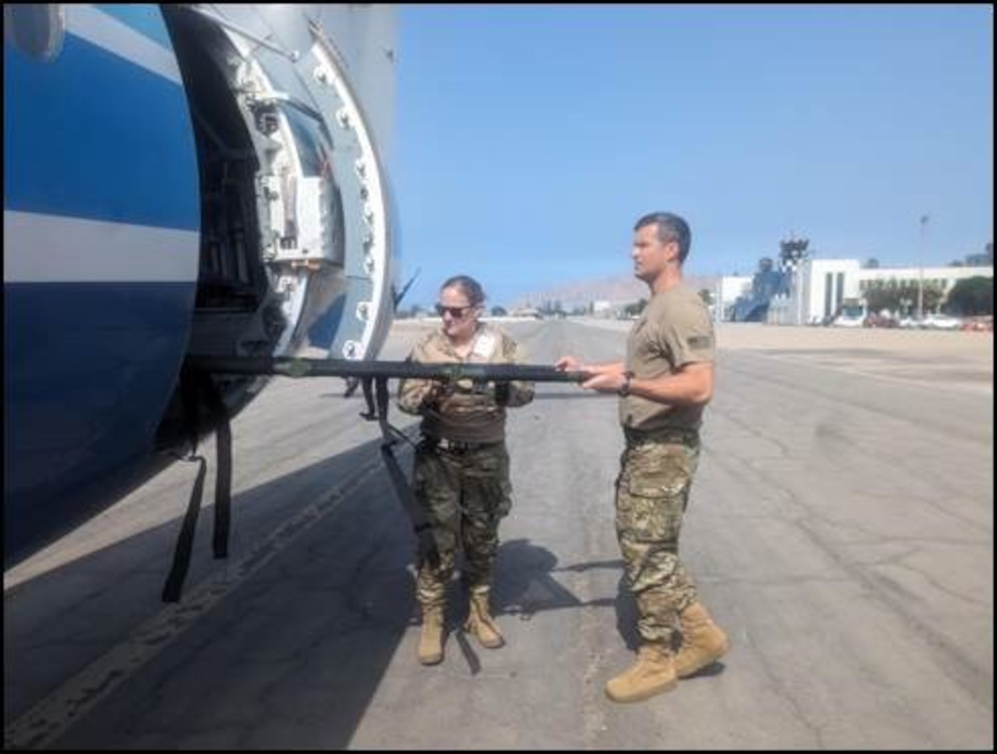 Two airmen lift a causality evacuation litter transload into an aircraft.