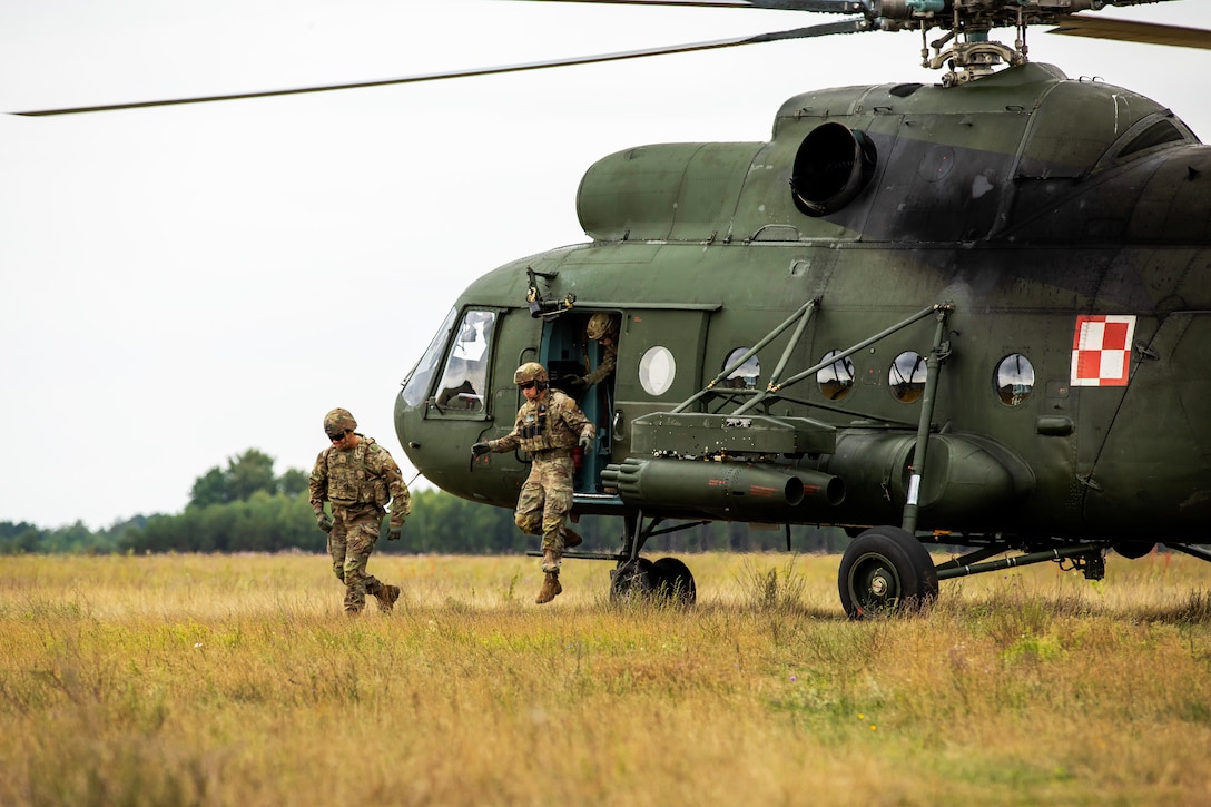 Soldiers exit a helicopter in a field.