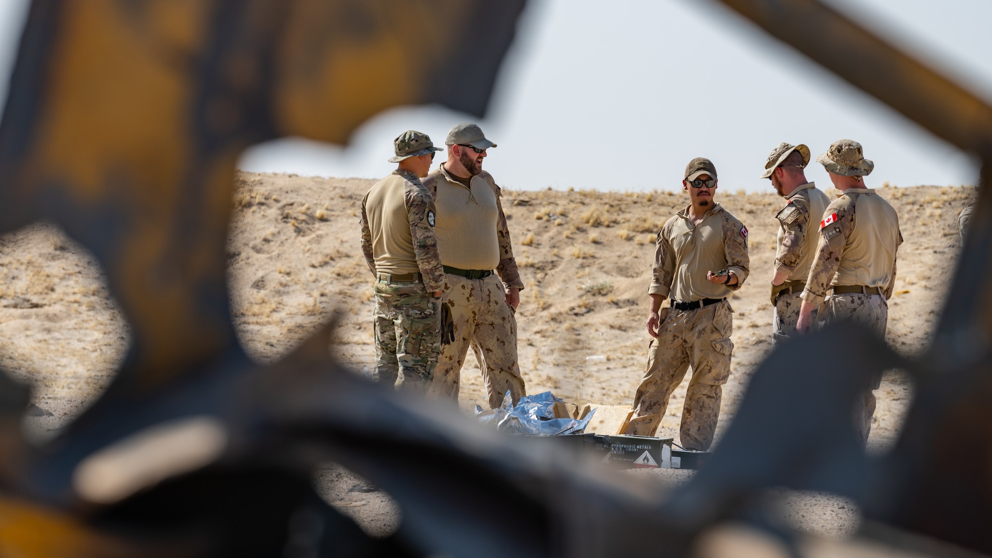 A U.S. Air Force explosive ordnance disposal (EOD) technician from the 386th Expeditionary Civil Engineer Squadron, left, talks to Canadian armed forces members about the explosives that will be used during a controlled detonation near Ali Al Salem Air Base, Kuwait, July 21, 2023. EOD technicians from the 386th ECES frequently work with our coalition partners during demolitions like this to destroy various hazardous materials in a safe and controlled environment. (U.S. Air Force photo by Staff Sgt. Kevin Long)