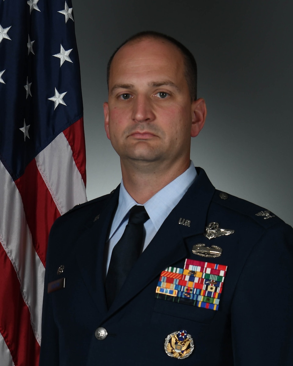 Headshot photo of man in military uniform with United States flag in the background