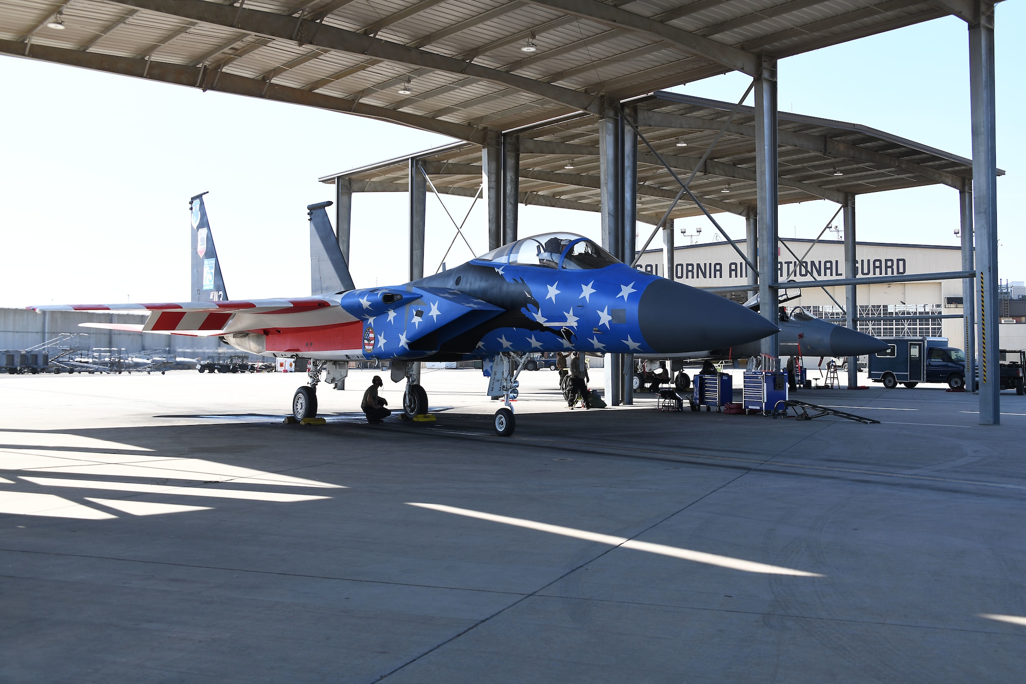 An F-15C fighter jet with a red, white, and blue paint scheme is parked under an aircraft bay.