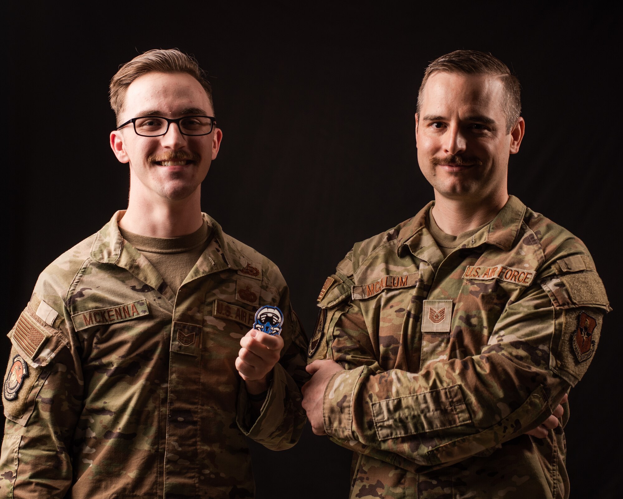 U.S. Air Force Staff Sgt. Parker McKenna (left) and Tech. Sgt. Anthony McAlum (right), Luke Air Force Base Air Force Gaming ambassadors, pose for a photo with the official AFG coin, July 19, 2023, at Luke AFB, Arizona.
