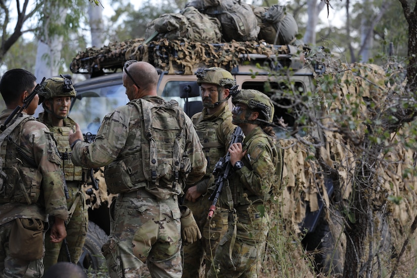 Multiple uniformed service members gather outside a vehicle.