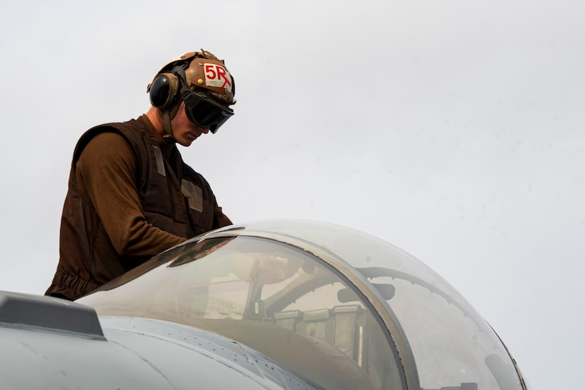A sailor wearing goggles cleans an aircraft.