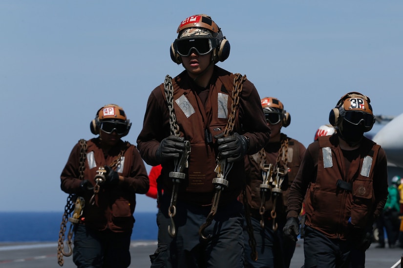 Sailors carrying chains walk aboard a ship.