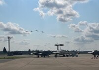 photo of four A-10Cs flying over an airborne warning and control system aircraft and two A-10Cs on the flight line.