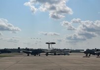 photo of four A-10Cs flying over an airborne warning and control system aircraft and two A-10Cs on the flight line.