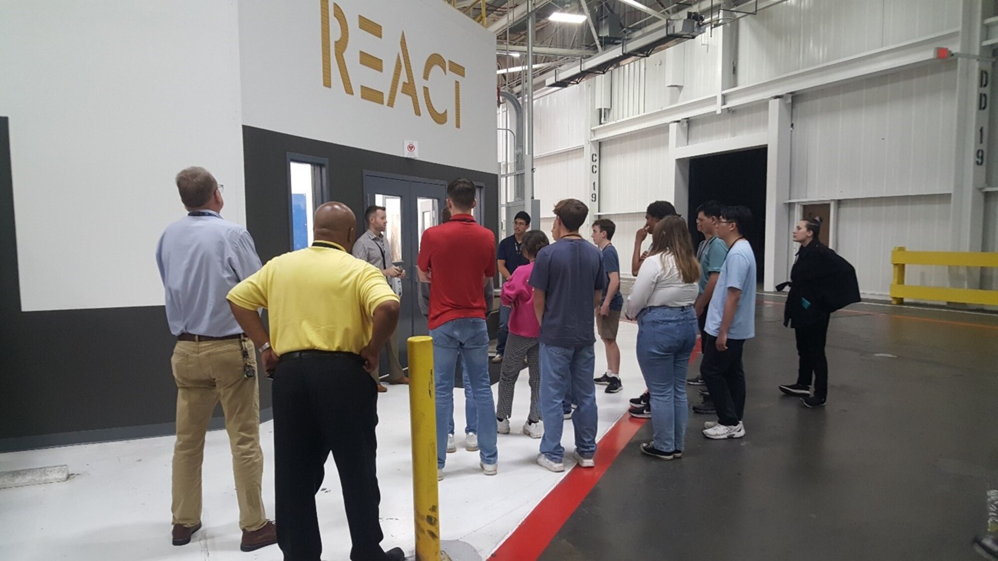 A group of students and adults stand in front of the entrance to a laboratory