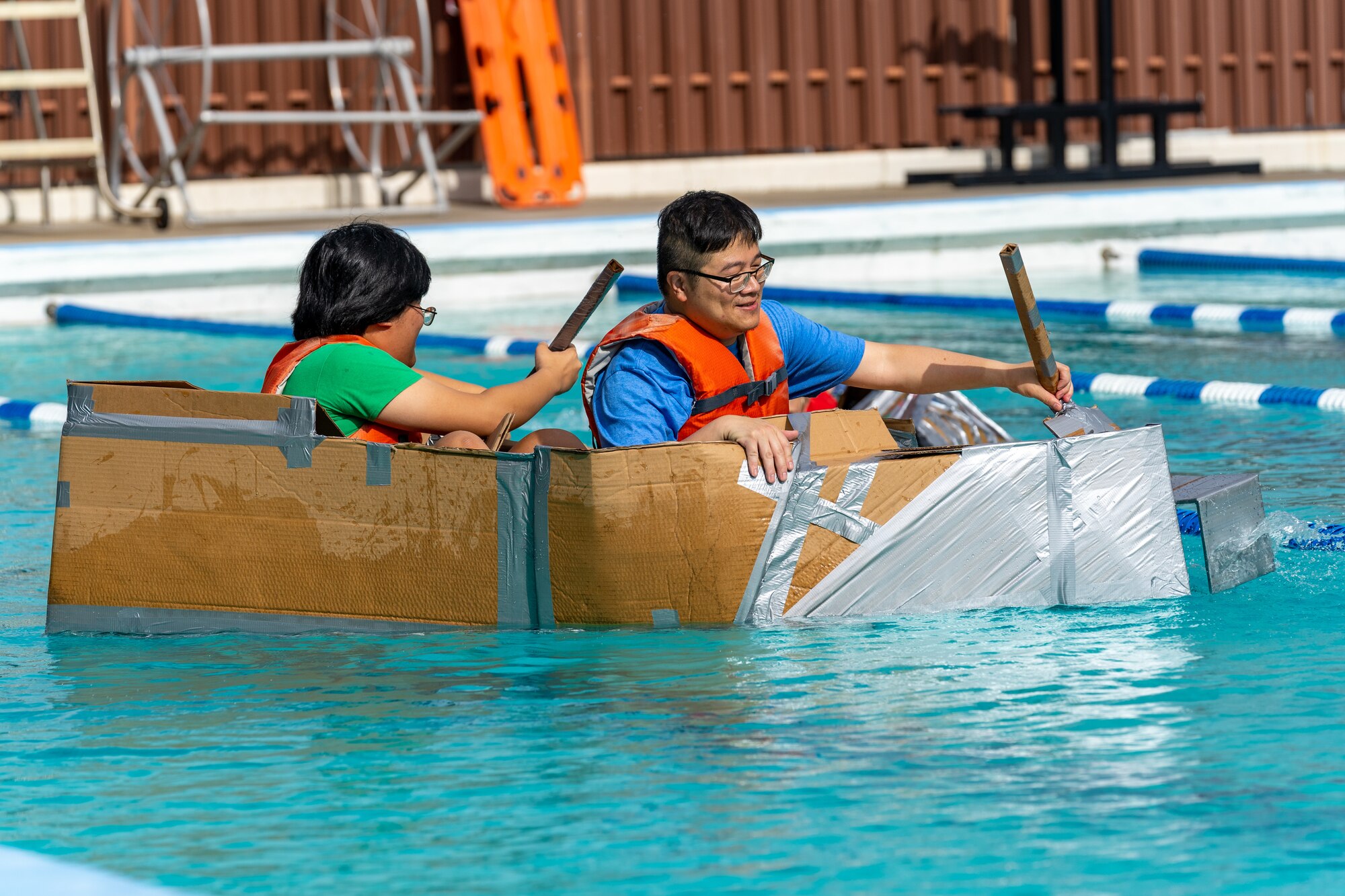 U.S. Navy Chief Funsing Cool, Ingalls Shipbuilding supervisor of shipbuilding, and Matthew Cool paddle their boat during the Cardboard Regatta at Keesler Air Force Base, Mississippi, July 15, 2023.