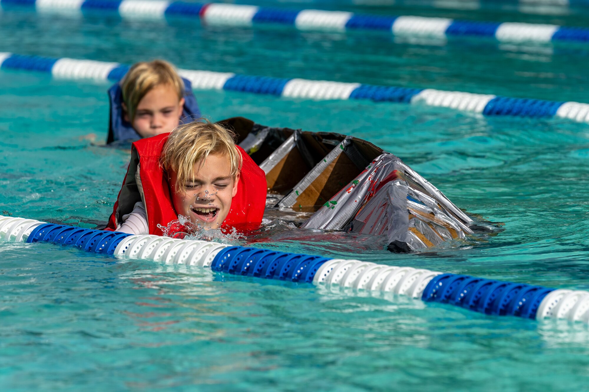 Carson and Chance Belgard swim with their boat during the Cardboard Regatta at Keesler Air Force Base, Mississippi, July 15, 2023.