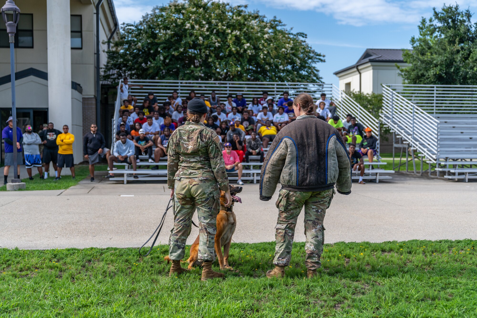 U.S. Air Force Staff Sgt. Ryan Wood and Airman 1st Class Tessa Spare, 81st Security Forces Squadron military working dog trainers, and Victor, 81st SFS MWD, perform a demonstration for Columbus High School student at Keesler Air Force Base, Mississippi, July 17, 2023.