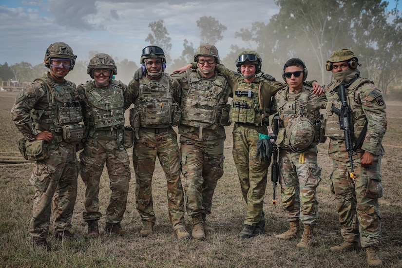 Seven service members wearing battle gear pose for a photo outdoors.