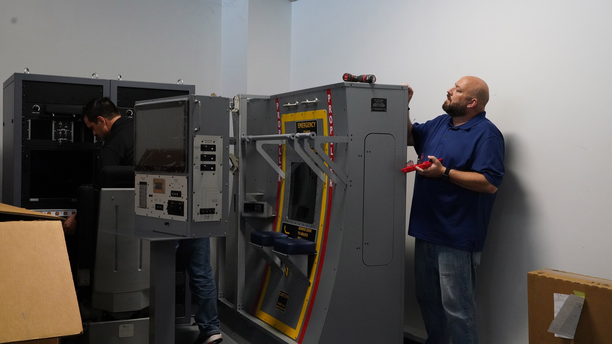 Two civilian males from the 502nd Trainer Development Flight work together to set up the new weather officer static trainer.