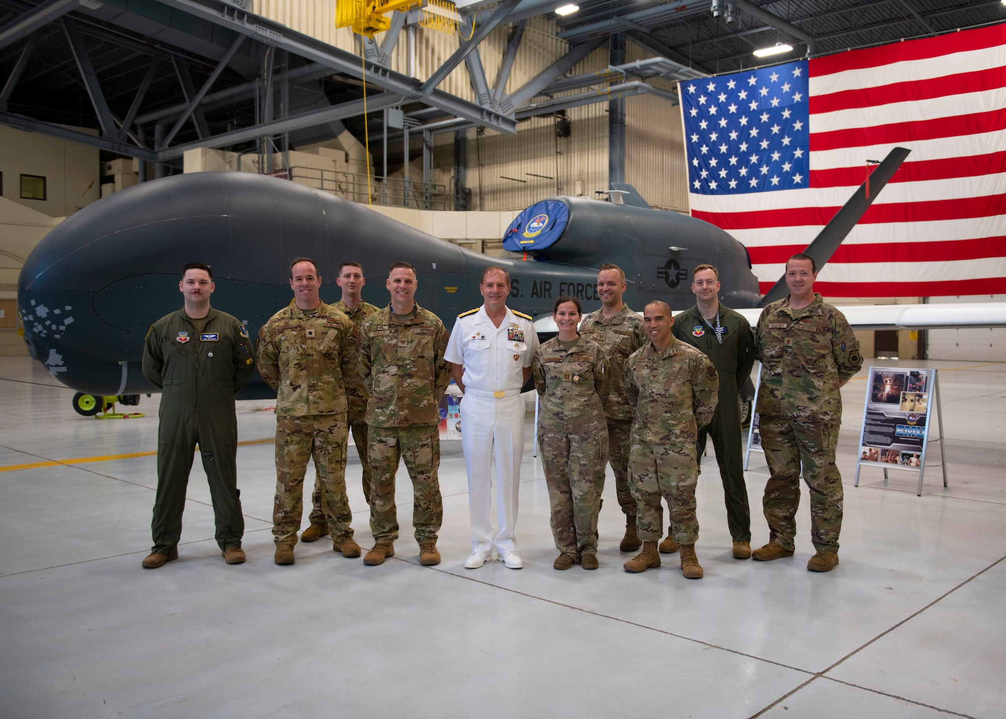 Service members stand in front of an aircraft and the U.S. flag smiling for a photograph.