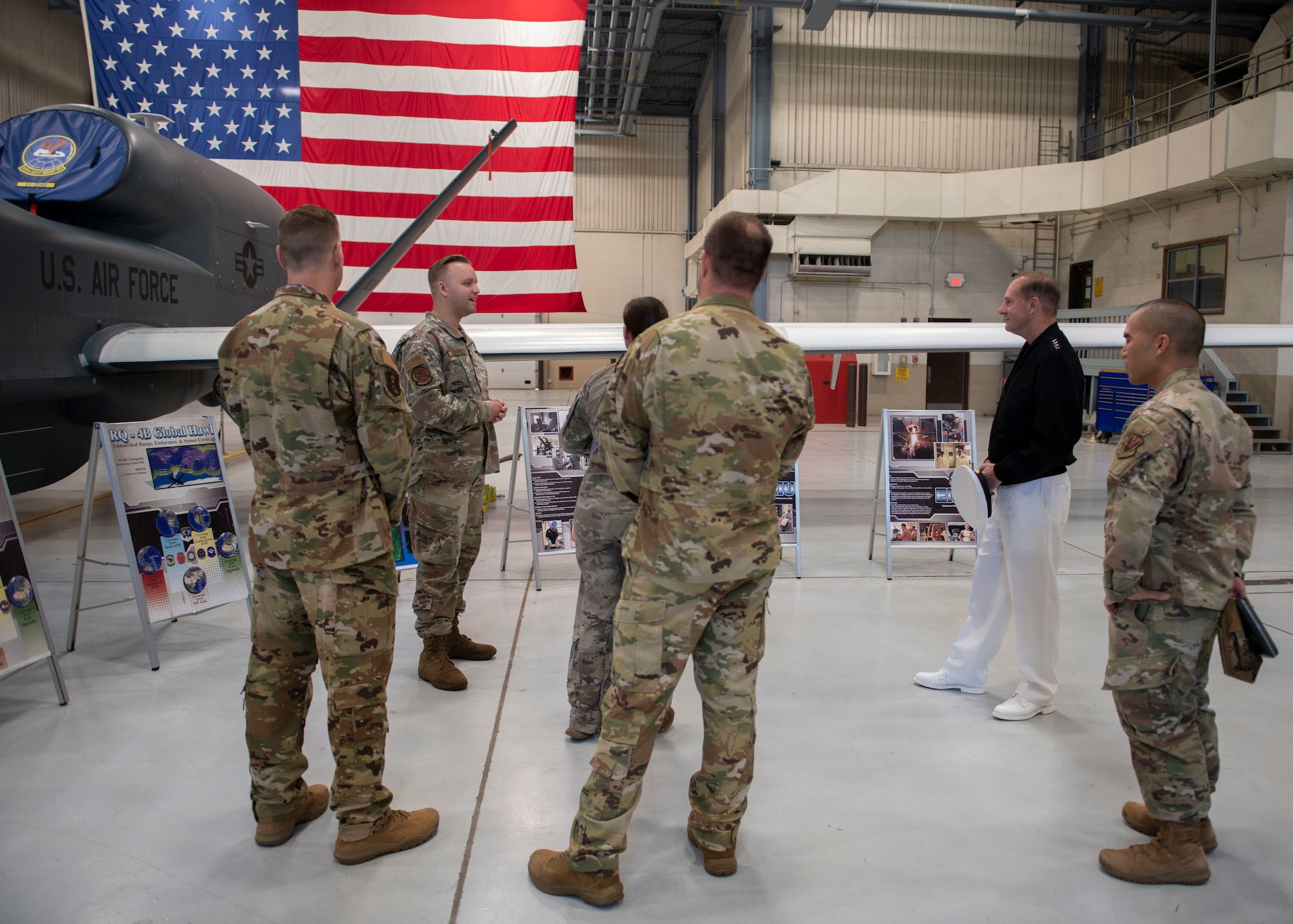 Service members stand near an aircraft and the U.S. flag in a hangar.