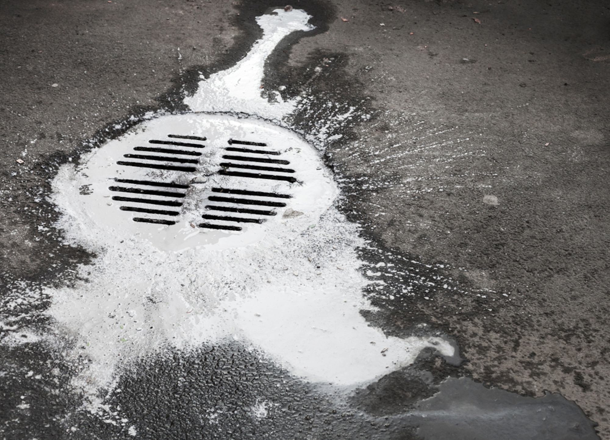 Black and white photo of a street drainage with paint spilled around it.