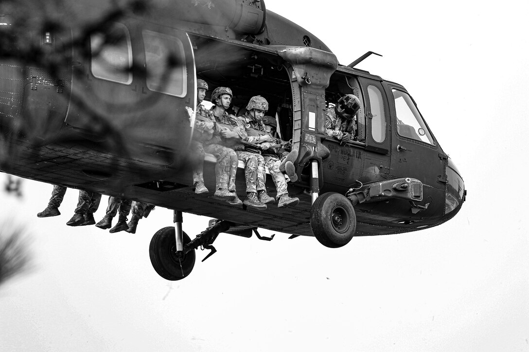 Army paratroopers look down from a military helicopter in this black and white photo.