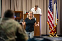 Woman is standing speaking to another man with a man in the background at a podium