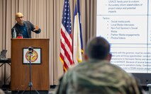 Man stands at podium on a stage talking to another man