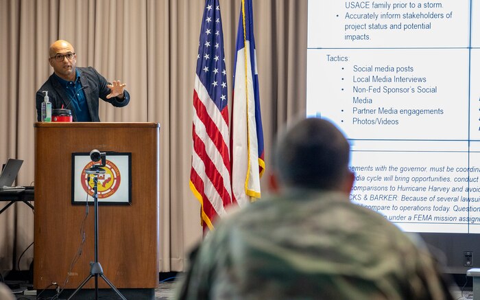 Man stands at podium on a stage talking to another man