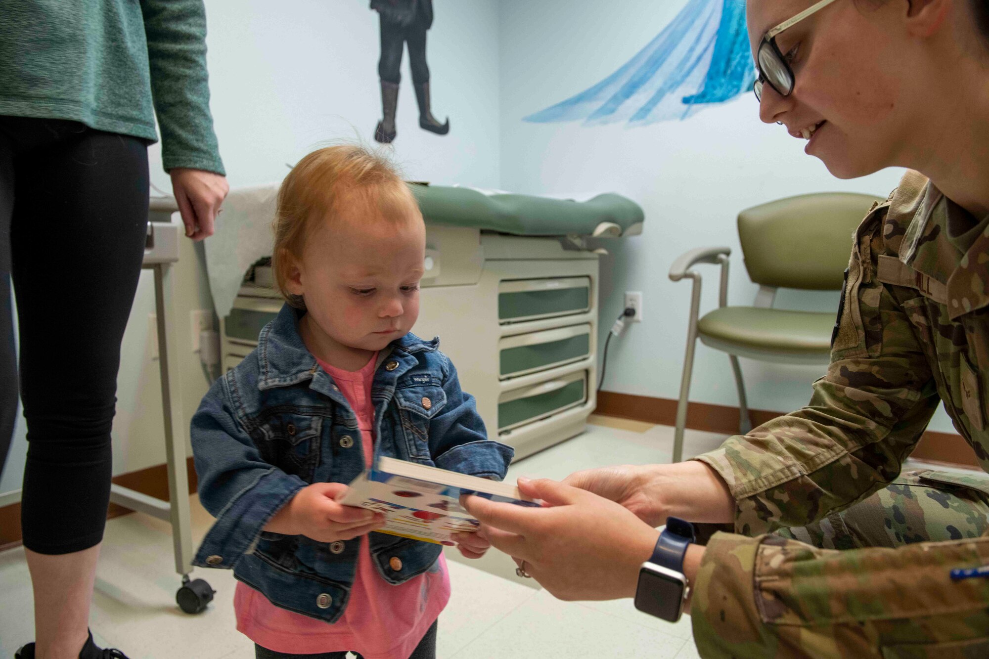 U.S. Air Force Airman 1st Class Madelyn Wall, 9th Healthcare Operations Squadron aerospace medical service technician, gives a book to Emerson Hales for the Reach Out and Read Initiative during a clinical visit at the pediatrics clinic June 19, 2023, at Beale Air Force Base, California.