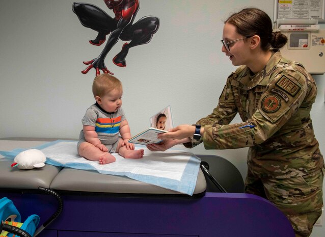 U.S. Air Force Airman 1st Class Madelyn Wall, 9th Healthcare Operations Squadron aerospace medical service technician, gives a book to Oliver Carson for the Reach Out and Read Initiative during a clinical visit at the pediatrics clinic June 19, 2023, at Beale Air Force Base, California.