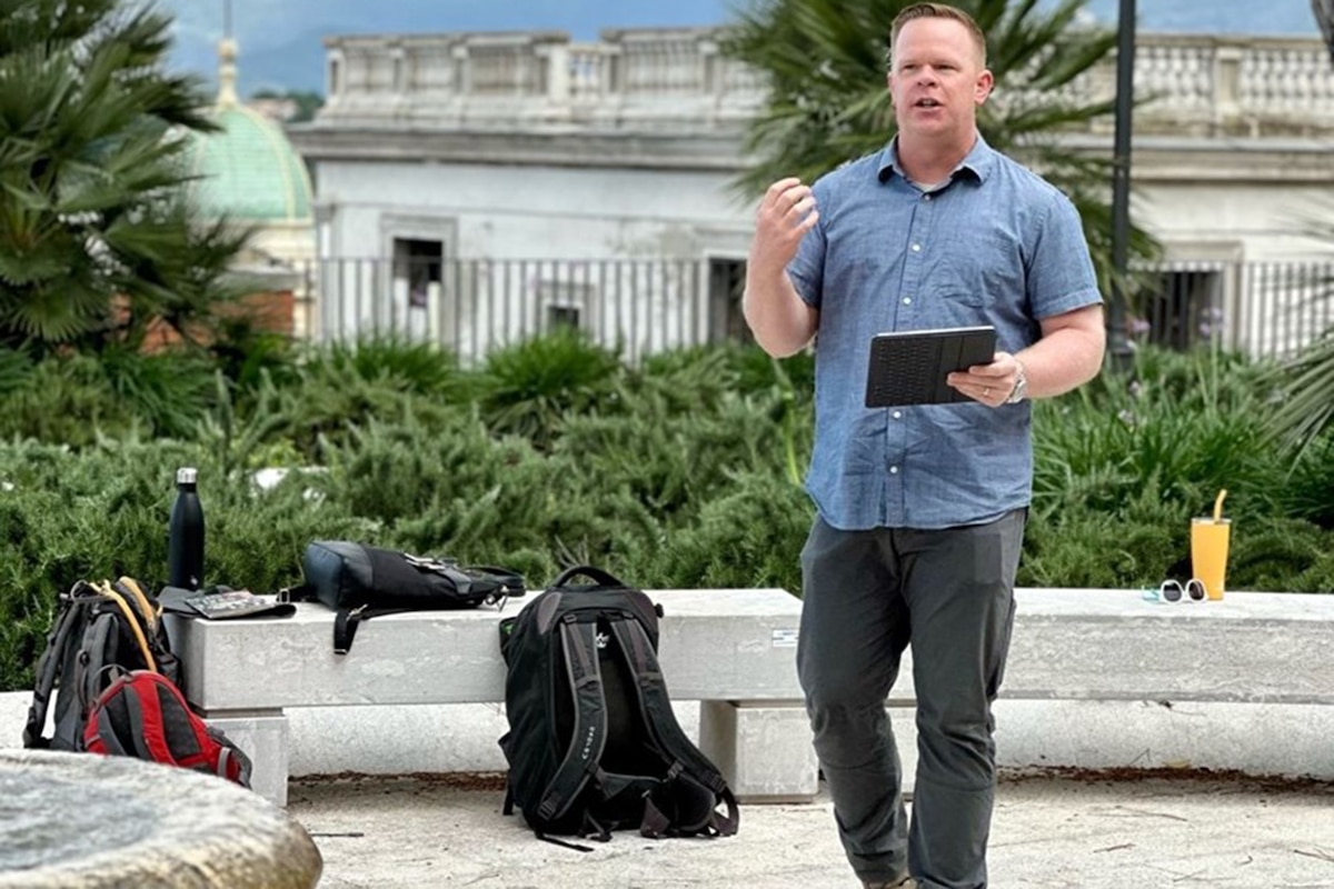 A man holds an electronic device and speaks.
