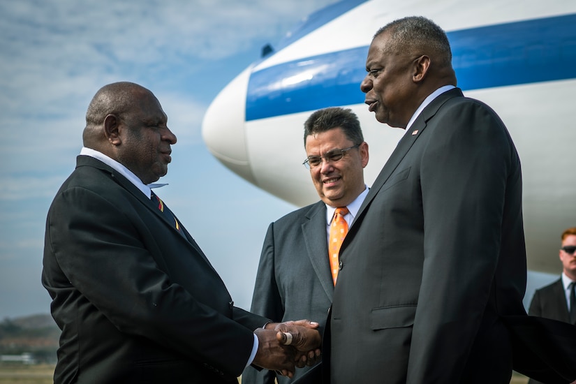 Two men shake hands while a third looks on.