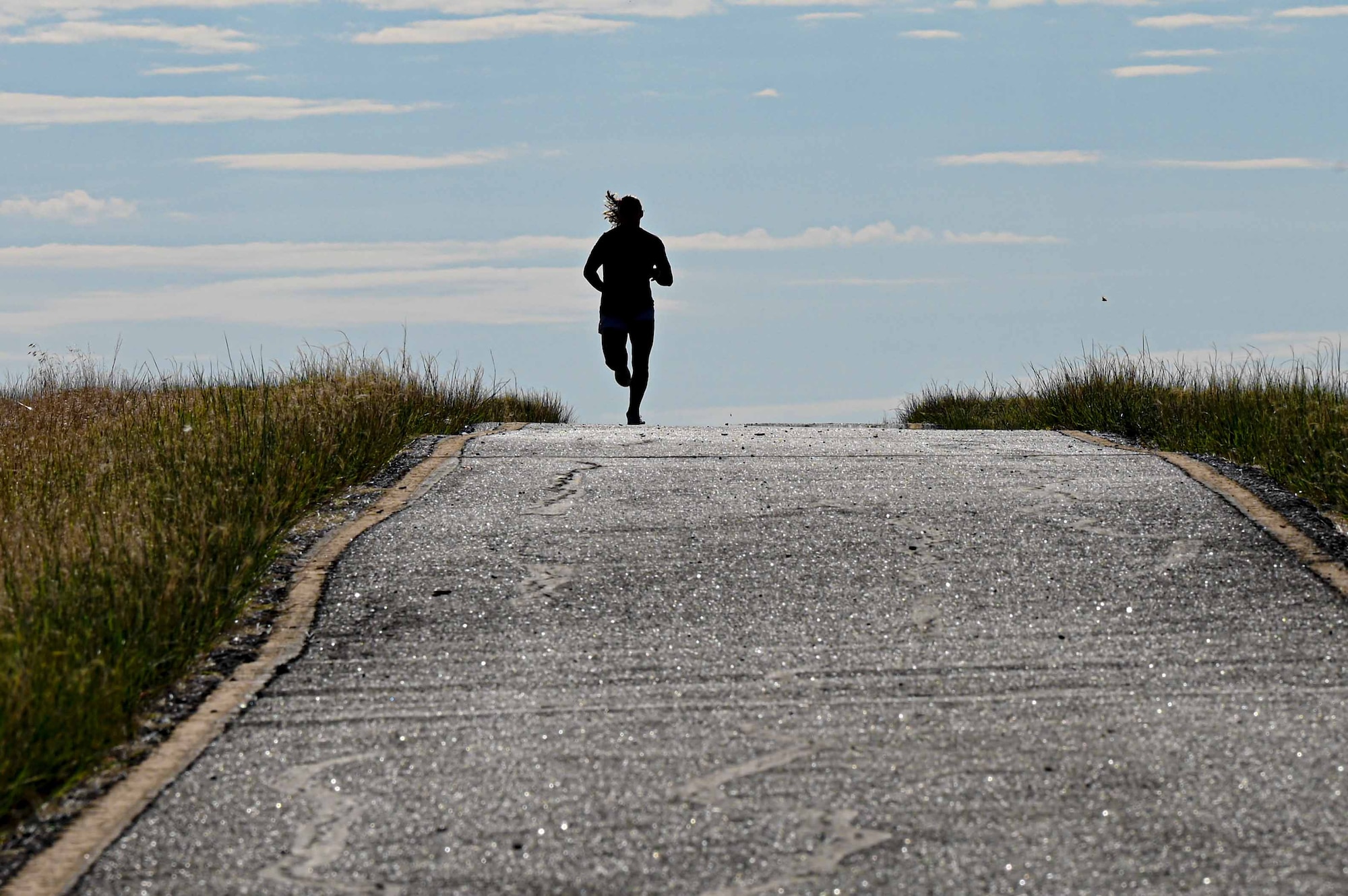 A silhouette of a woman is shown as she runs on a trail