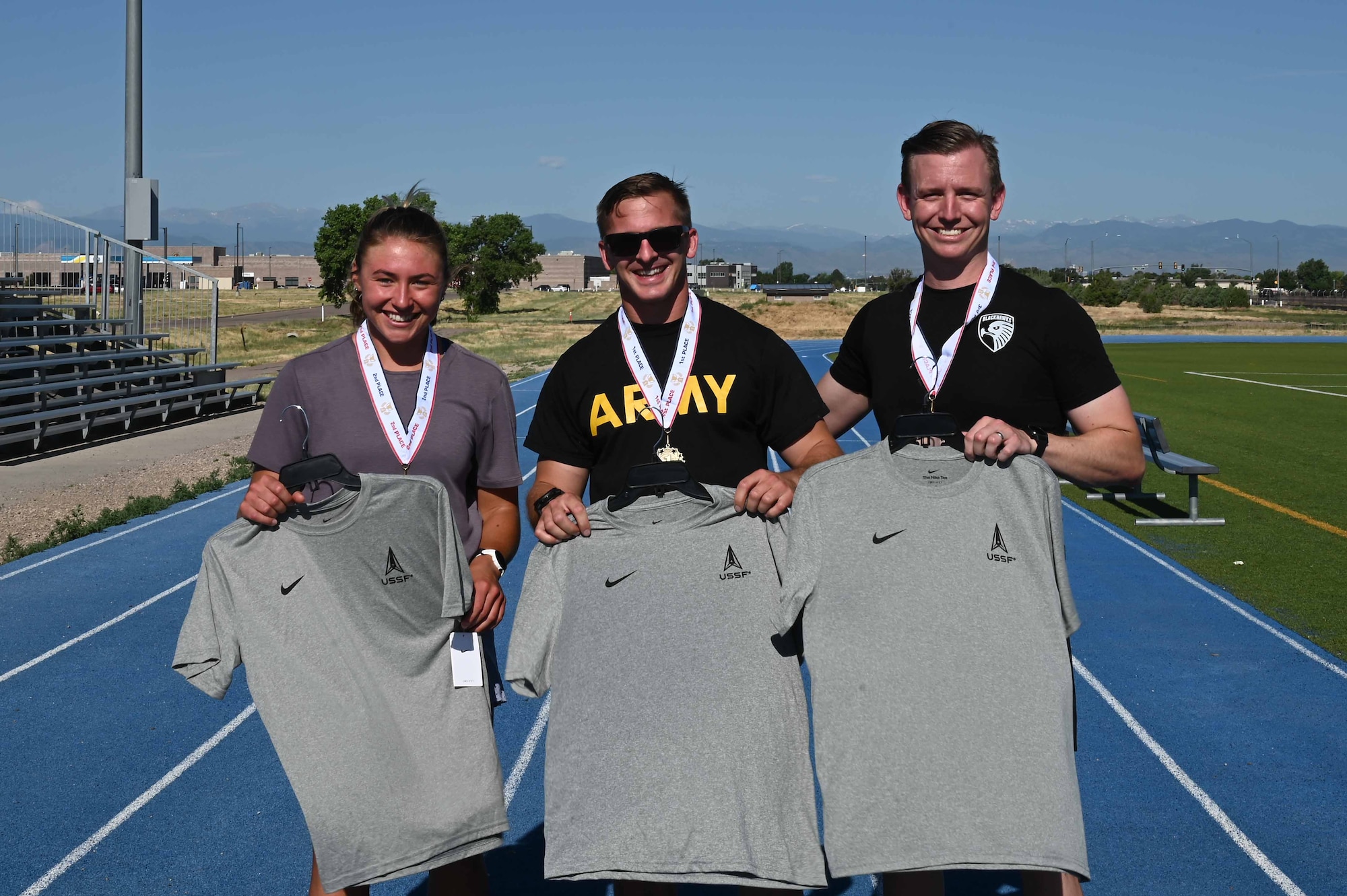 Three winners of a race pose on a track with their medals and Space Force t-shirts