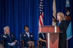 A woman talks at a lectern while others sit in chairs behind her.