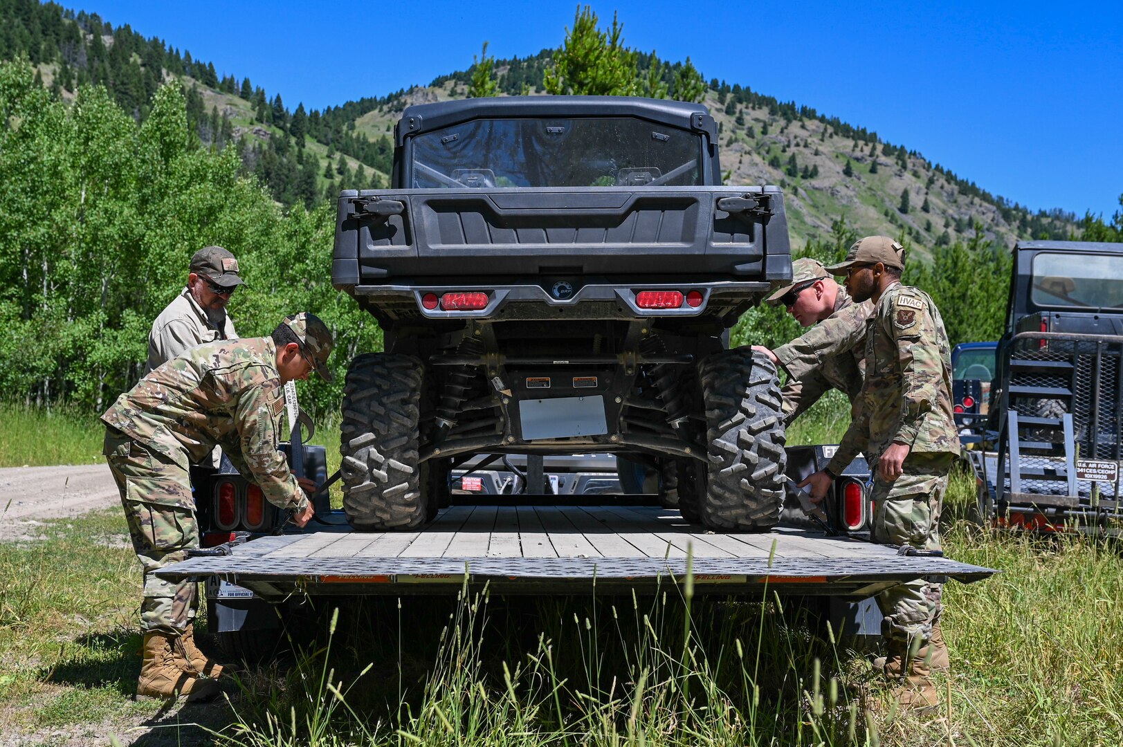 Four people tighten a vehicle to a trailer