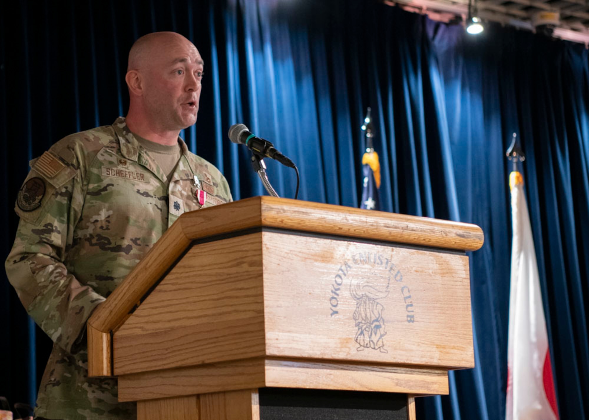 Military man stands behind a podium on stage.